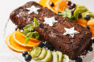 Chocolate brownie cake with fresh blueberries, white stars made of powdered sugar, orange slices, kiwi and mint leaves. Homemade cake decorated with fruit. Festive concept