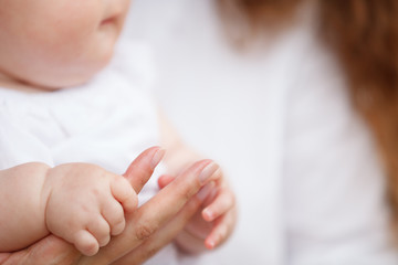 Mother uses her hand to hold her baby's tiny hand to make him feeling her love, warm and secure.