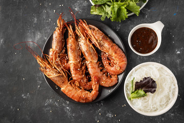 Fried grilled prawns with rice noodle, sauce and lettuce, dark background,copy space