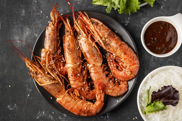 Fried grilled prawns with rice noodle, sauce and lettuce, dark background,
