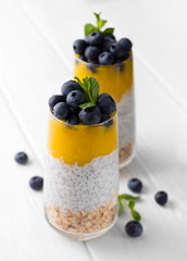 Glass of yogurt with chia seed, blueberries and mango mousse and oatmeal on a white wooden table.