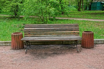  brown wooden bench and a urn are standing on an alley in the park among green grass and trees