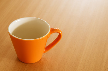 Empty orange colored cup on a wooden table.