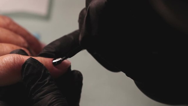 Manicure, nail lacquer, gel. The master makes a decorative manicure gel with a varnish. dark blue color of varnish, tight blue tone. Hands close-up, against the background of a yellow towel