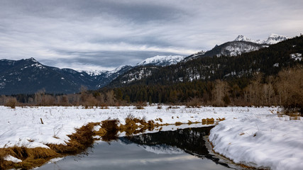 A creek winds through a winter landscape toward snow peaked mountains in west Montana