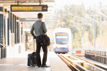 Businessman business traveler commuter with roller bag suitcase waiting on train station platform
