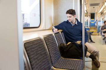 Young professional man commuter using cell phone riding on light rail subway train