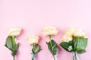 Fototapeta premium Beautiful fresh cut beige Roses in glass vase on pink background. Minimal floral composition for romantic gift, flat lay