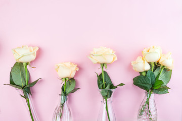 Beautiful fresh cut beige Roses in glass vase on pink background. Minimal floral composition for romantic gift, flat lay