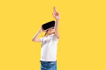 Girl 7 y.o. experiencing VR headset game on yellow background. Surprised emotions on her face.Child using a gaming gadget for virtual reality.Futuristic goggles at young age. Virtual technology