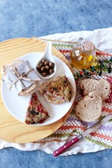 Plato con bocadillo y trozos de tortilla de psito, aceitunas, rebanadas de pan y aceitera con aceite, sobre paño de crochet.