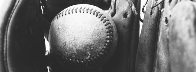 Close up of old vintage baseball in used worn leather glove, black and white sports banner.