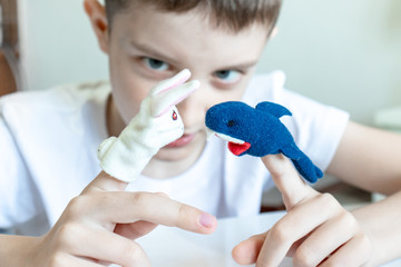 A caucasian boy playing different roles by using finger puppets, toys for expressing his emotions,...
