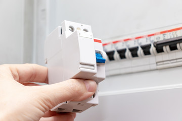 Hand holding new automatic switch and blurred electrical shield with automatic switches of...