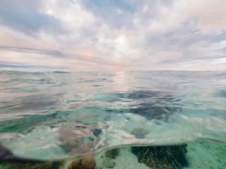 Transparent sea water and cloudy sky landscape waterline view. Coral reef on seabed in crystal clear sea water and cloudy blue sky splitted by waterline. Natural background.