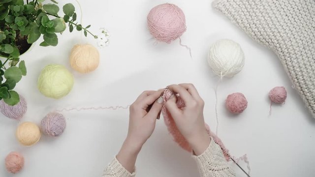 Female hands knit from pink yarn with steel needles.