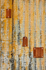 Rusty sheet of corrugated metal wall with metal patches, as an orange textured background