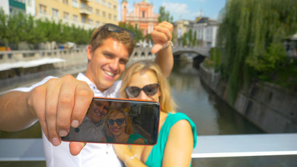 CLOSE UP Adorable tourist couple smile and wave at the phone during a skype call
