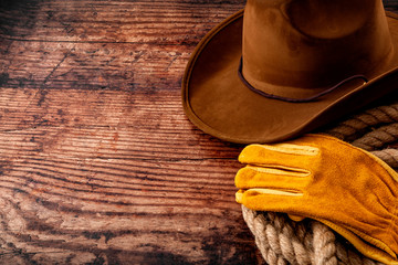American culture, living on a ranch or farm and country muisc concept theme with a cowboy hat, rope lasso and rodeo leather gloves on a wooden background in a old saloon with copy space - obrazy, fototapety, plakaty