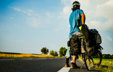 Cyclotourist facing backward and looking at a long road ahead of him