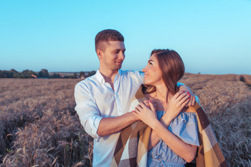 Young couple man woman summer wheat field happy smiling hugging, caring covering blanket relaxing. Concept love, date, emotion, tenderness, warmth, care, romance. Happiness hugs lovers, young family.