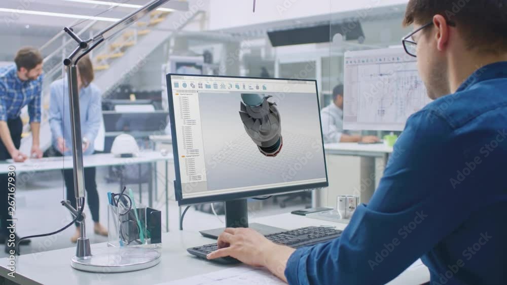 Fototapete Engineer Working on Desktop Computer, Screen Showing CAD Software with 3D Engine Prototype. In the Background Engineering Facility with Blueprints and Drawings. Over the Shoulder