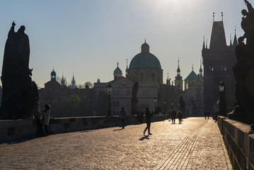 Outdoor silhouette view of people or tourist enjoy beautiful sunny day on Charles Bridge, and background of Old Town Bridge Tower and Church of St. Salvator in the morning in Prague, Czech Republic. 
