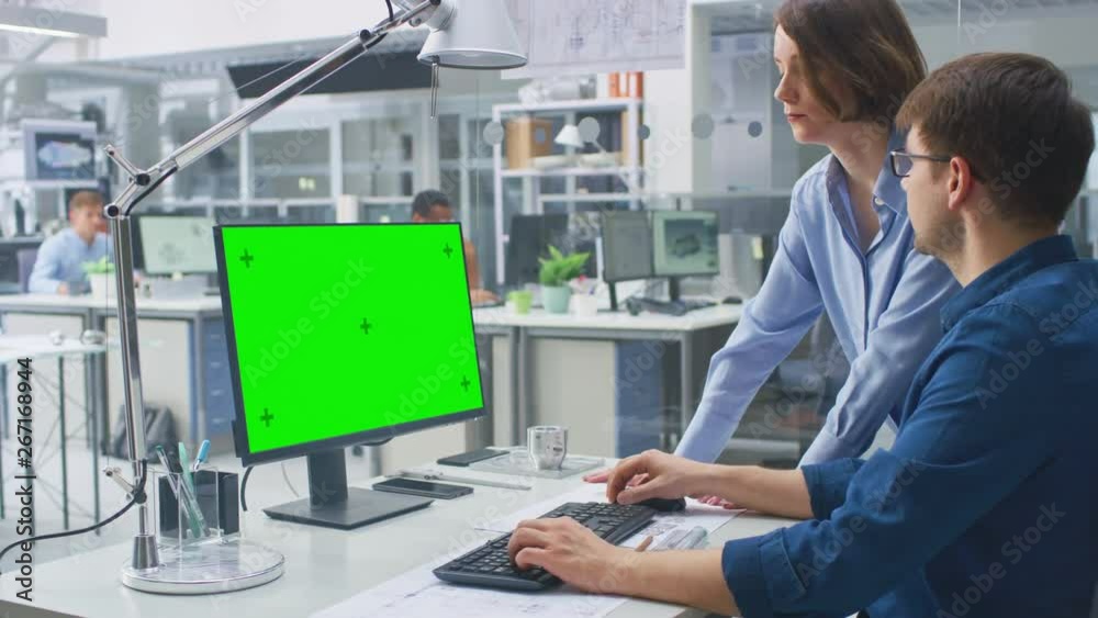 Poster Engineer Working with Green Mock-up Screen Desktop Computer Is advised by Female Project Manager. Engineering Facility with Specialists Working on Blueprints and Drawings with Industrial Design