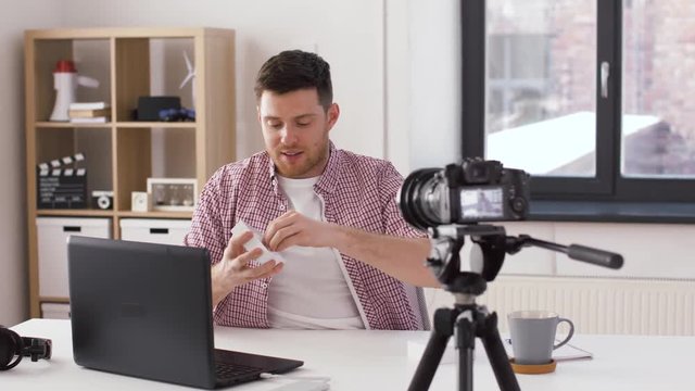 blogging, videoblog and people concept - male blogger with camera opening box and recording video review of new wireless earphones in charging case at home