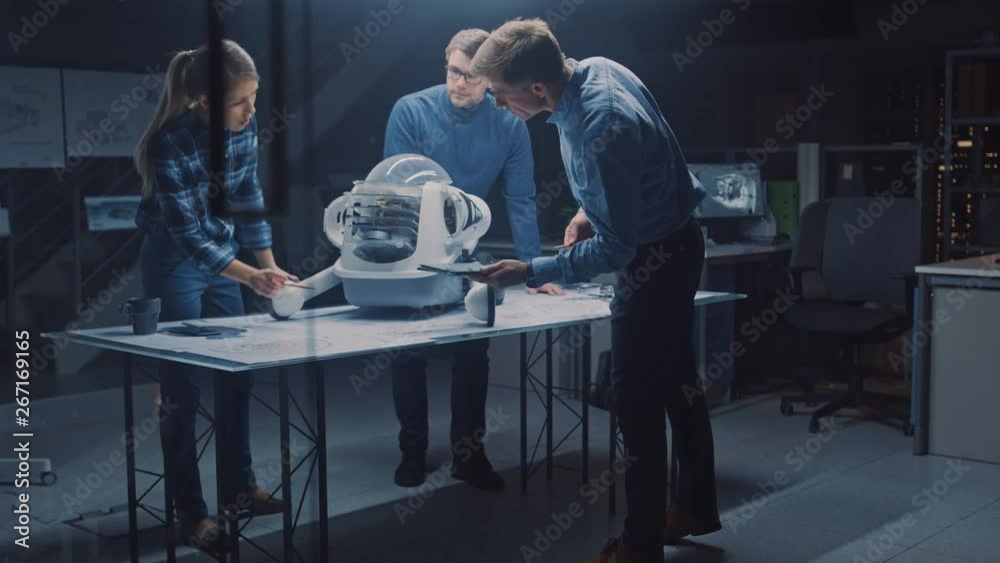 Leinwandbilder Robotics Engineering Facility Three Technical Engineers Talk and Work on Wheeled Robot Prototype. In the Background High Tech Research Center with Screens Showing Industrial Design. Focusing Dark Shot