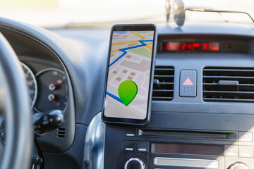 Obraz premium The map on the phone in the background of the dashboard. Black mobile phone with map gps navigation fixed in the mounting. App map for travel.