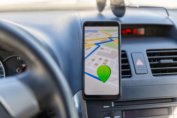 Fototapeta premium Arrival or destination point on the map in the phone on the dashboard background. Black mobile phone with GPS map navigation is fixed in the installation. App map for traveling with route
