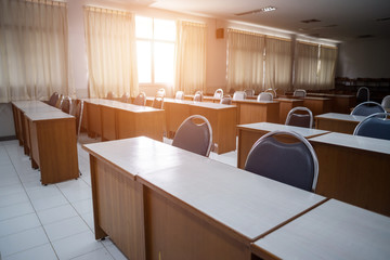 Education concept: Empty college or university classroom with wooden tables and chairs in row without student or teacher in the room. School classroom with window opened, clean and tidy ready for new 