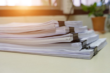 Education concept: Close and selective focus of unfinished homework assignment stack archives with binder paper clips on teacher’s desk in university waiting to be evaluated and scored. Stack of white