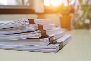 Education concept: Close and selective focus of unfinished homework assignment stack archives with binder paper clips on teacher’s desk in university waiting to be evaluated and scored. Stack of white