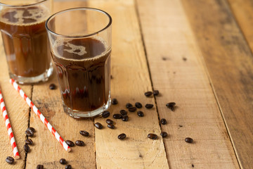 Iced iced coffee in large transparent glasses, poured over milk, with coffee beans on a wooden background, summer cooling drink, with copy space