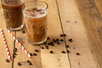 Iced iced coffee in large transparent glasses, poured over milk, with coffee beans on a wooden background, summer cooling drink, with copy space