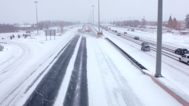 Team of huge snowplows clear highway/freeway in a blizzard. During a blizzard, snowplows are clearing the snow followed by a traffic jam pileup of cars. 