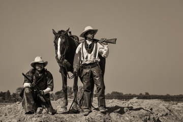 Vintage photo, of two men wearing a cowboy outfit with a horse and a gun held in the hand.