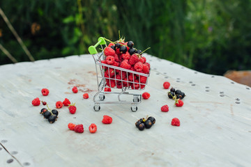 Mini shopping basket full of fresh red ripe raspberry and blackberry on vintage background