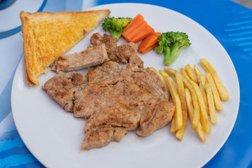 Kurobuta pork chop with vegetable and french fries in white dish.