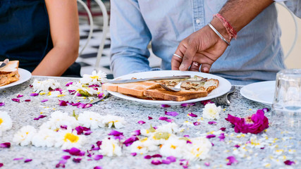 Obraz na płótnie Canvas Waiter brings breakfast toasts and pancakes to a couple sitting at the table covered with flowers petals in hotel. Table close-up.