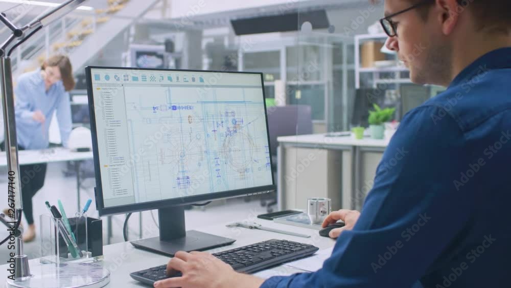 Poster Over the Shoulder Shot of Engineer Working with CAD Software on Desktop Computer, Screen Shows Technical Drafts and Drawings. In the Background Engineering Facility Specialising on Industrial Design