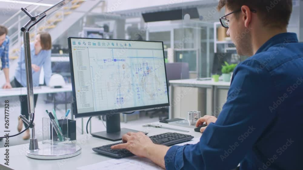 Poster Over the Shoulder Shot of Engineer Working with CAD Software on Desktop Computer, Screen Shows Technical Drafts and Drawings. In the Background Engineering Facility Specialising on Industrial Design