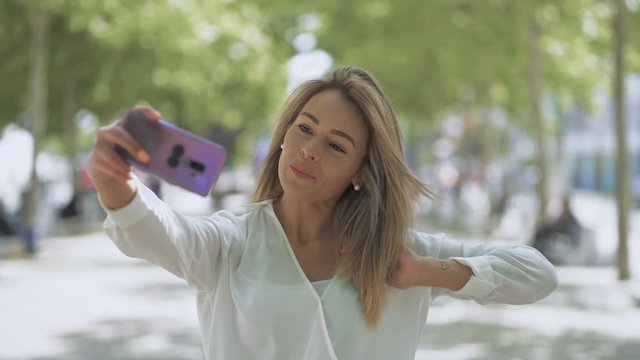 Attractive smiling girl taking selfie outdoor. Beautiful happy young woman taking selfie with smartphone on street. Taking picture concept