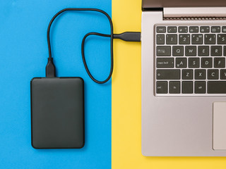 Black hard drive and laptop on yellow and blue background. Flat lay. The concept of backup storage.