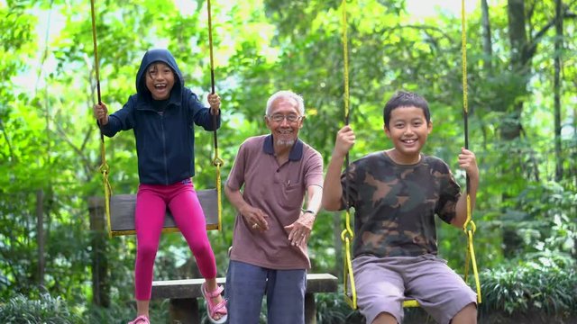 Joyful children and their grandfather playing on the swing at the park. Shot in 4k resolution