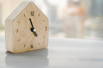 Wooden Home clock. five minutes to five o'clock in the morning . Wood clockwise on business building background. Time go Buy Home for Happy Life and overtime working concept