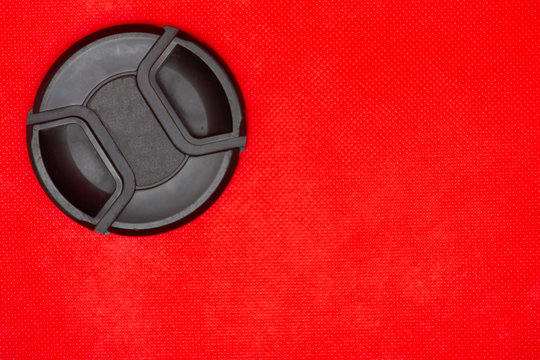 Black circle lens cap for DSLR camera lens on a rich red background.