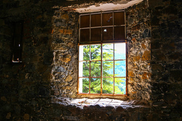 The structure of an old stone in the half-ruined house is looked through around a window aperture in beams of the midday sun.